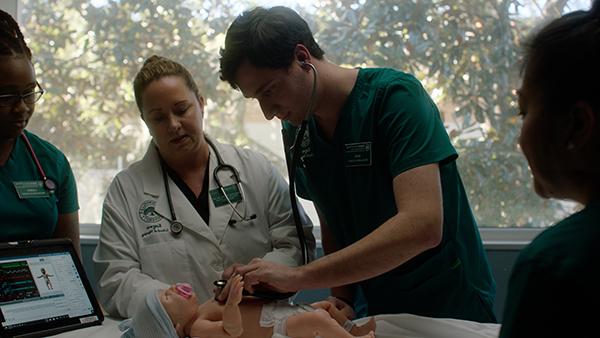 A student performs a simulation on a medical manikin with the aid of his teacher